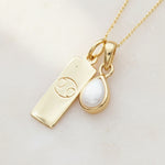 Gold necklace with a june birthstone pearl pendant and a cancer zodiac symbol pendant on a light background
