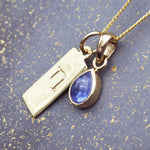 Gold necklace with a December birthstone tanzanite pendant and Capricorn zodiac pendant on a textured blue background