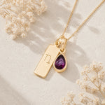 Gold necklace with a teardrop-shaped january birthstone natural garnet gemstone pendant and a rectangle pendant with capricorn line glyph on a light background