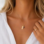Goldnecklace with a teardrop january birthstone natural garnet pendant and rectangle pendant with capricorn line glyph symbol on a person wearing a white shirt.