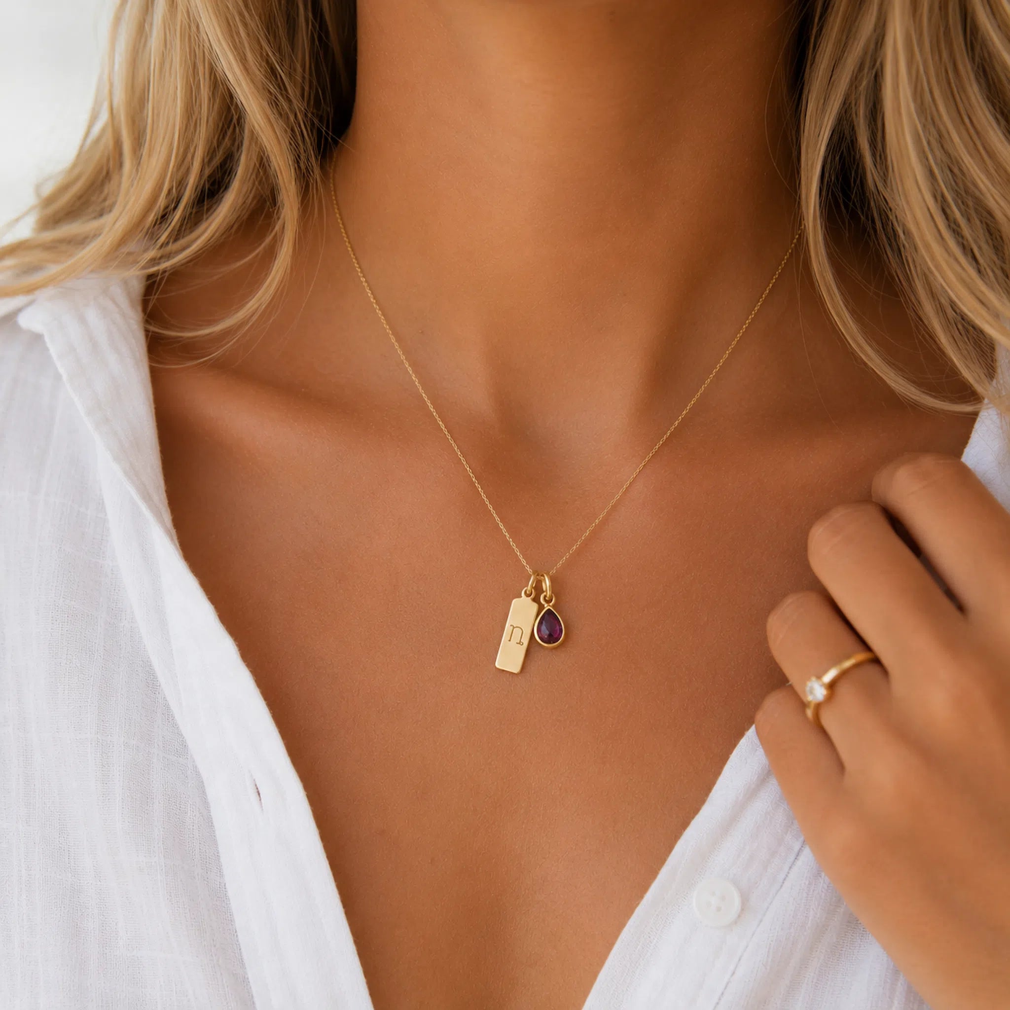Goldnecklace with a teardrop january birthstone natural garnet pendant and rectangle pendant with capricorn line glyph symbol on a person wearing a white shirt.