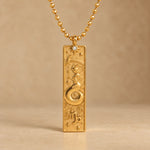 Gold Capricorn zodiac necklace, embossed bar pendant with sign symbol on a faceted ball chain, warm beige background