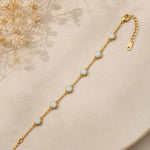 dainty gold chain bracelet with bezel set white opals on a light stone surface
