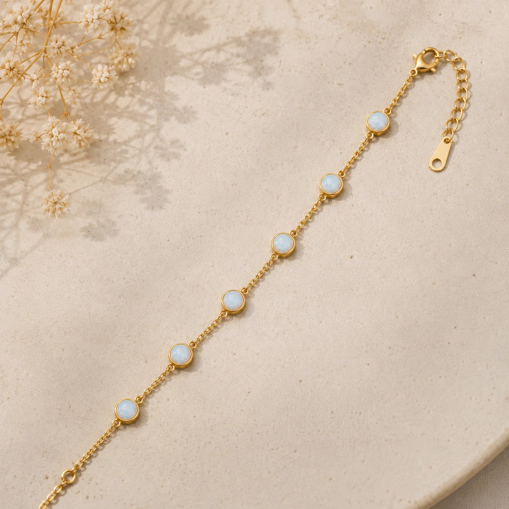 dainty gold chain bracelet with bezel set white opals on a light stone surface
