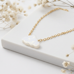 Gold necklace with a cloud shaped opal pendant on a white surface surrounded by small white flowers