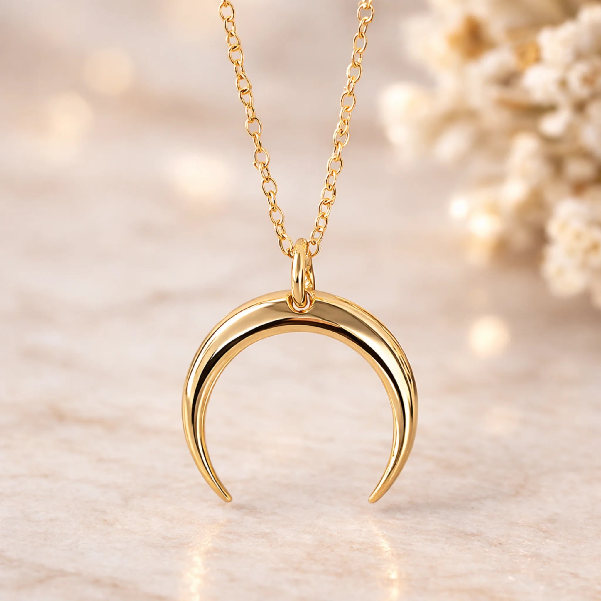 Gold crescent moon necklace on a soft beige background
