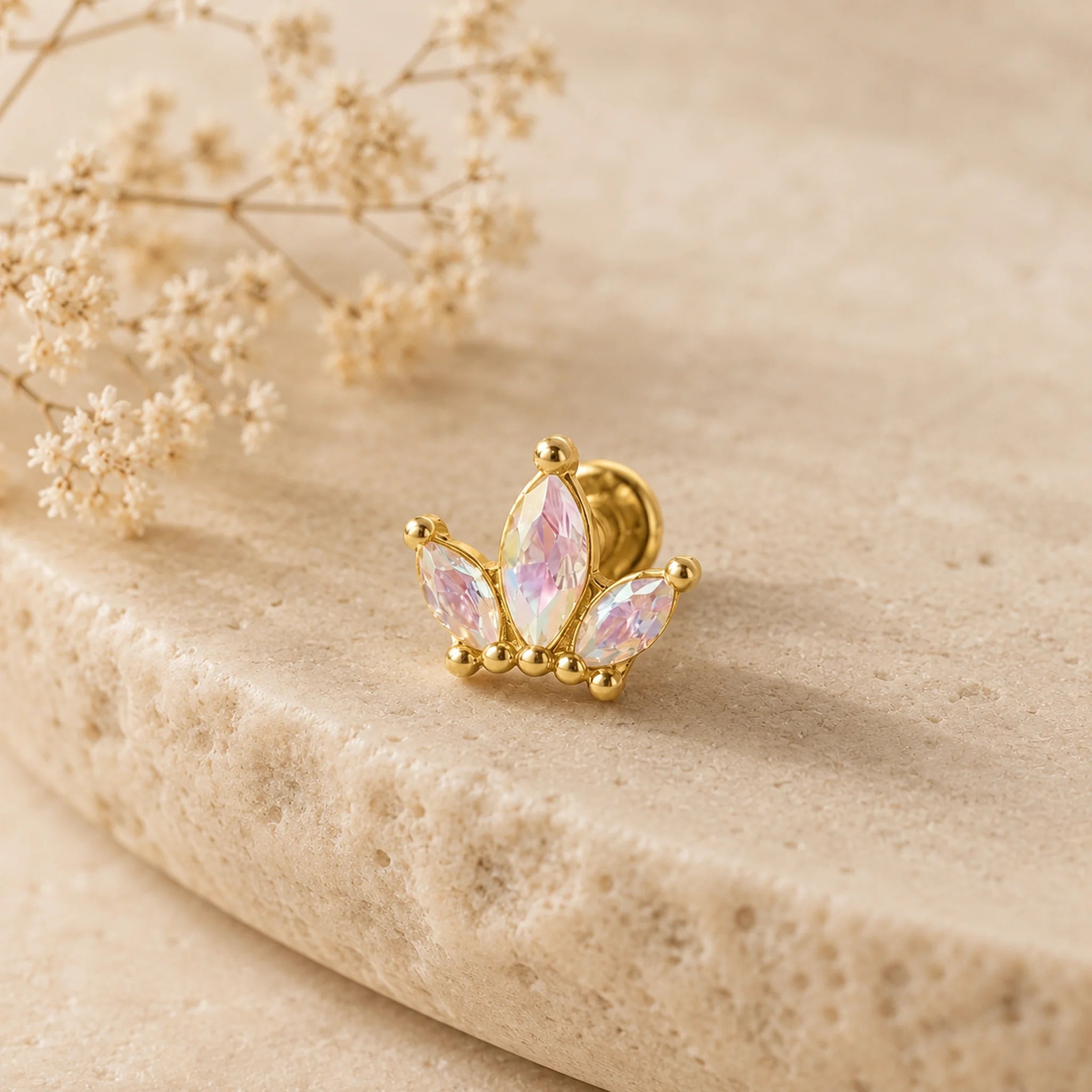 Gold earring with pink gemstones on a beige stone background