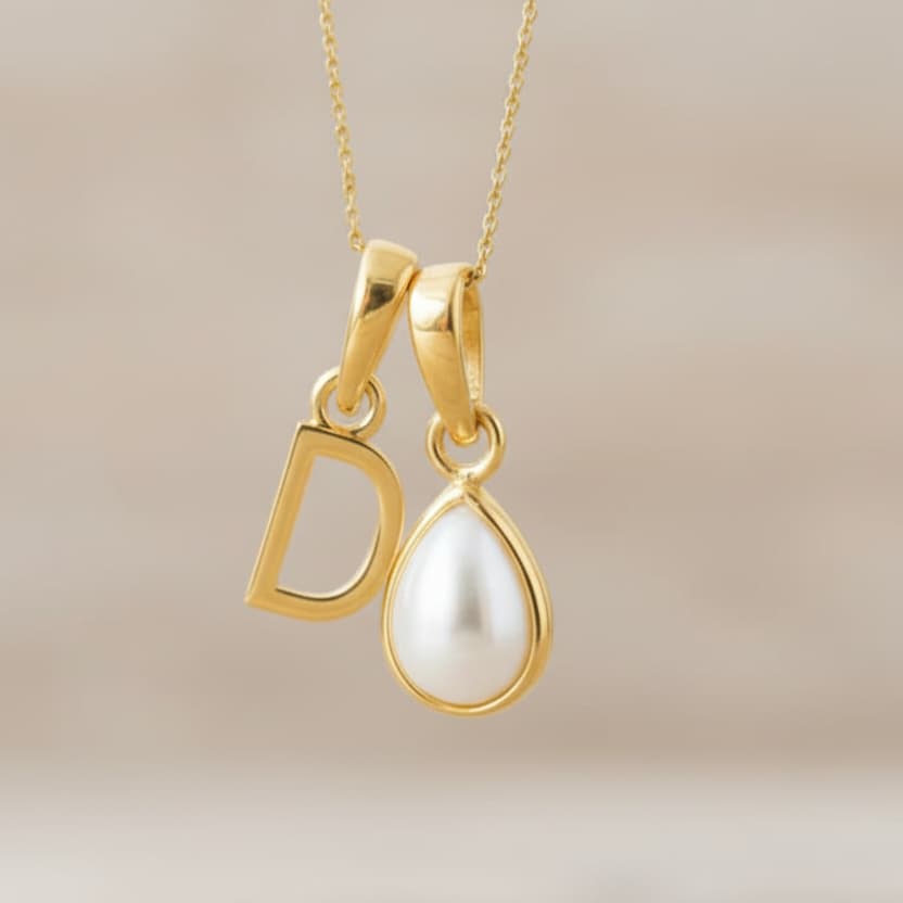 Gold pendant with 'D' and teardrop-shaped pearl on a beige background