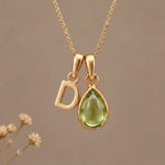 Gold Initial D Pendant and August birthstone Natural Peridot Necklace against a warm background