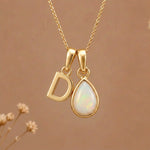 Gold Initial D Pendant and October birthstone Natural Opal Necklace against a warm background
