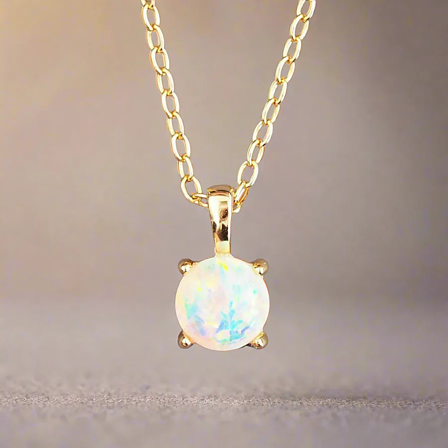 Gold necklace with a round opal pendant on a soft fabric background
