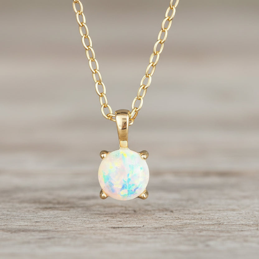 Gold necklace with a round opal pendant on a soft fabric background
