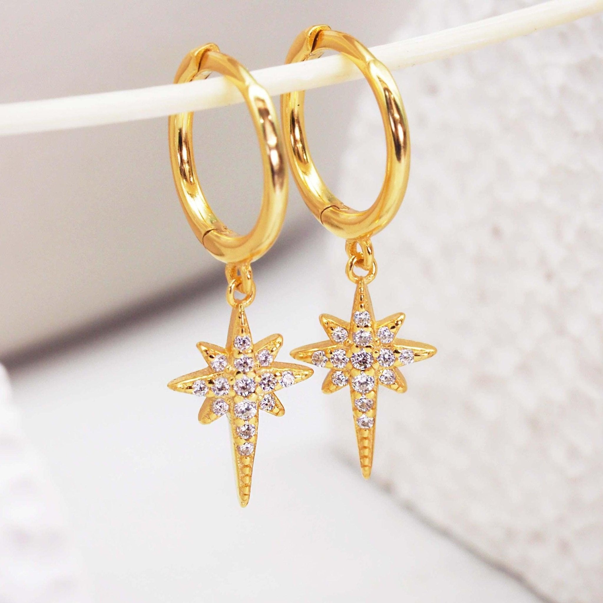 Gold hoop earrings with star-shaped charms with cubic zirconias on a light background