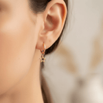 Gold hoop earring with a star charm worn by a person.