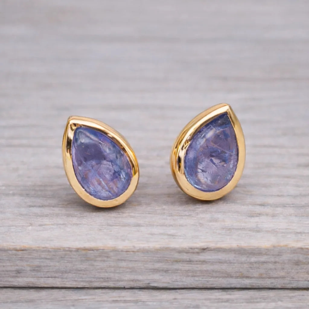 Teardrop-shaped tanzanite gemstone stud earrings in gold settings on a wooden surface