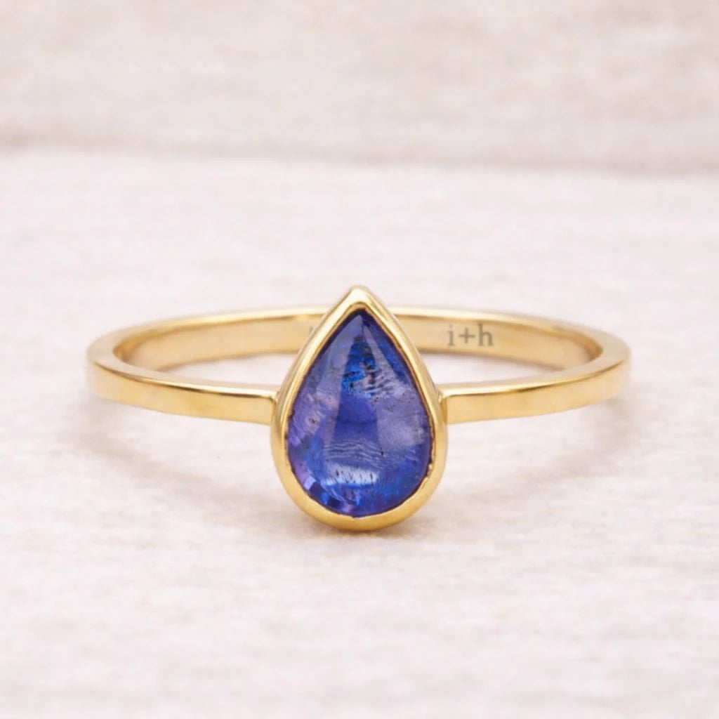 Gold ring with a blue teardrop-shaped natural tanzanite gemstone on a light background