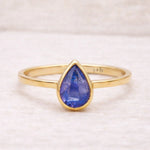 Gold ring with a blue teardrop-shaped natural tanzanite gemstone on a light background
