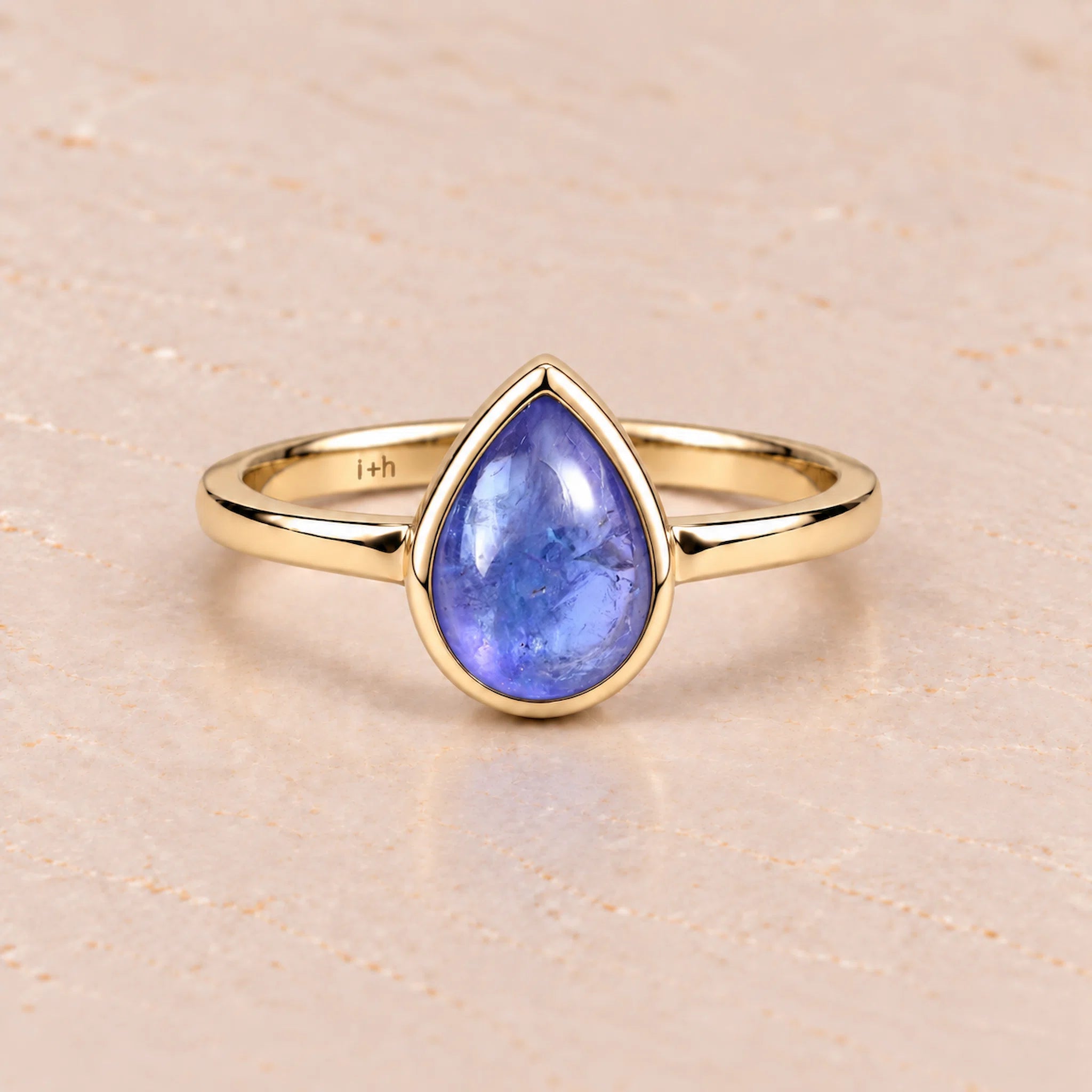 Gold december birthstone ring with a blue teardrop-shaped natural tanzanite gemstone on a light background