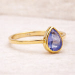 Gold ring with a teardrop-shaped natural tanzanite gemstone on a light background