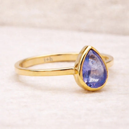 Gold ring with a teardrop-shaped natural tanzanite gemstone on a light background