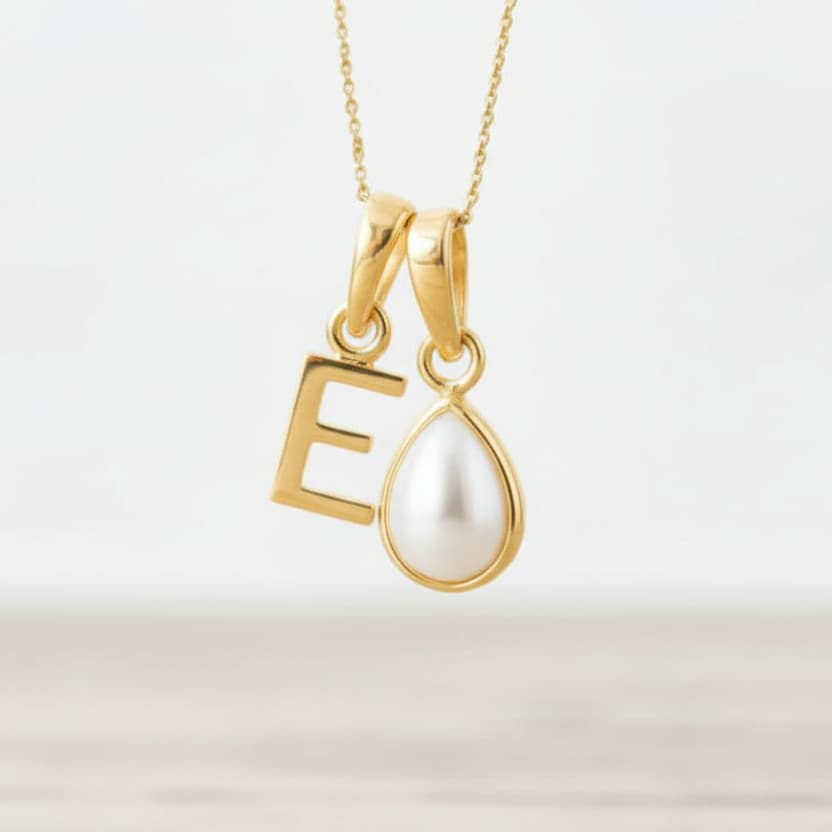 Gold necklace with 'E' pendant and teardrop-shaped pearl on a light background