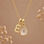 Gold initial E necklace with an April clear quartz teardrop on brown with dried flowers