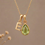 Gold Initial E Pendant and August birthstone Natural Peridot Necklace against a warm background