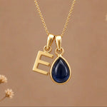 Gold Initial E Pendant and September birthstone Natural Sapphire Necklace against a warm background