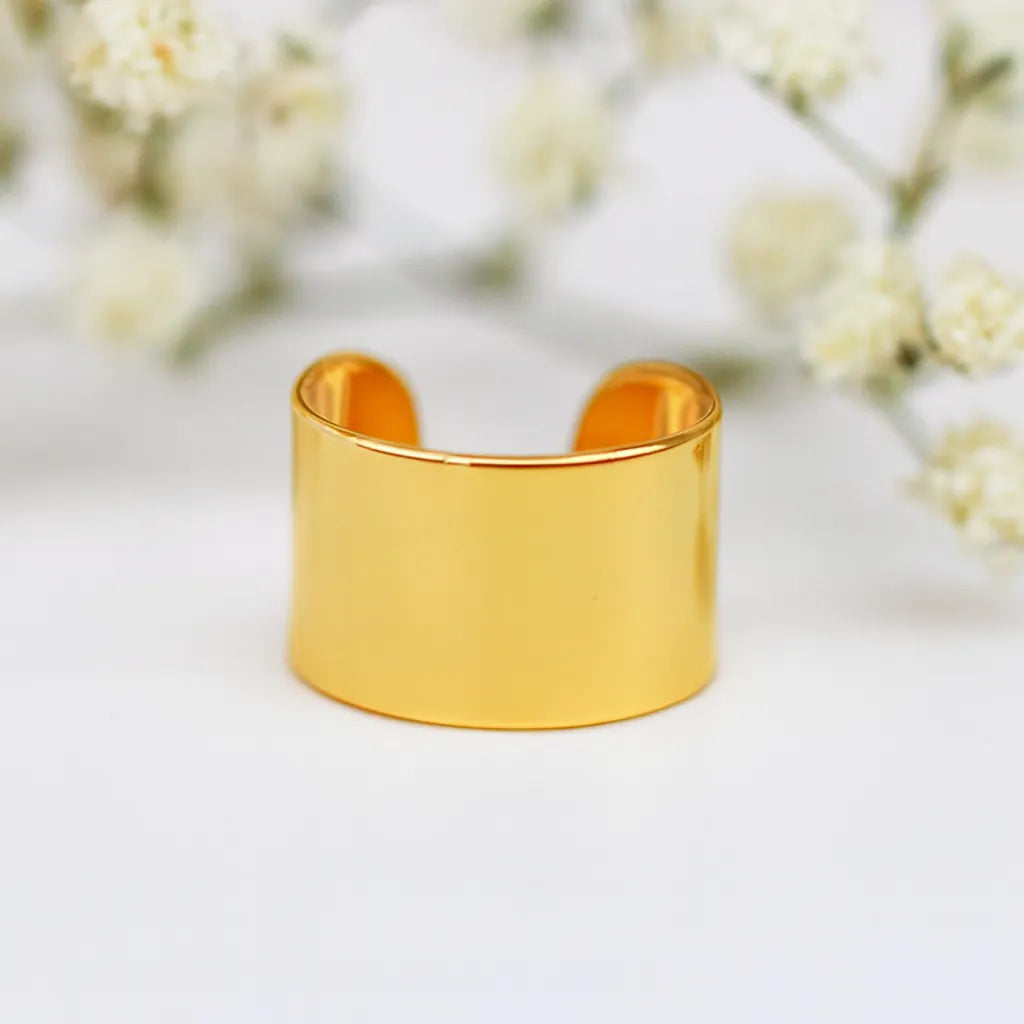 Gold ear cuff on a white background with blurred flowers in the background - gold waterproof jewellery by indie and harper