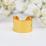 Gold ear cuff on a white background with blurred flowers in the background - gold waterproof jewellery by indie and harper
