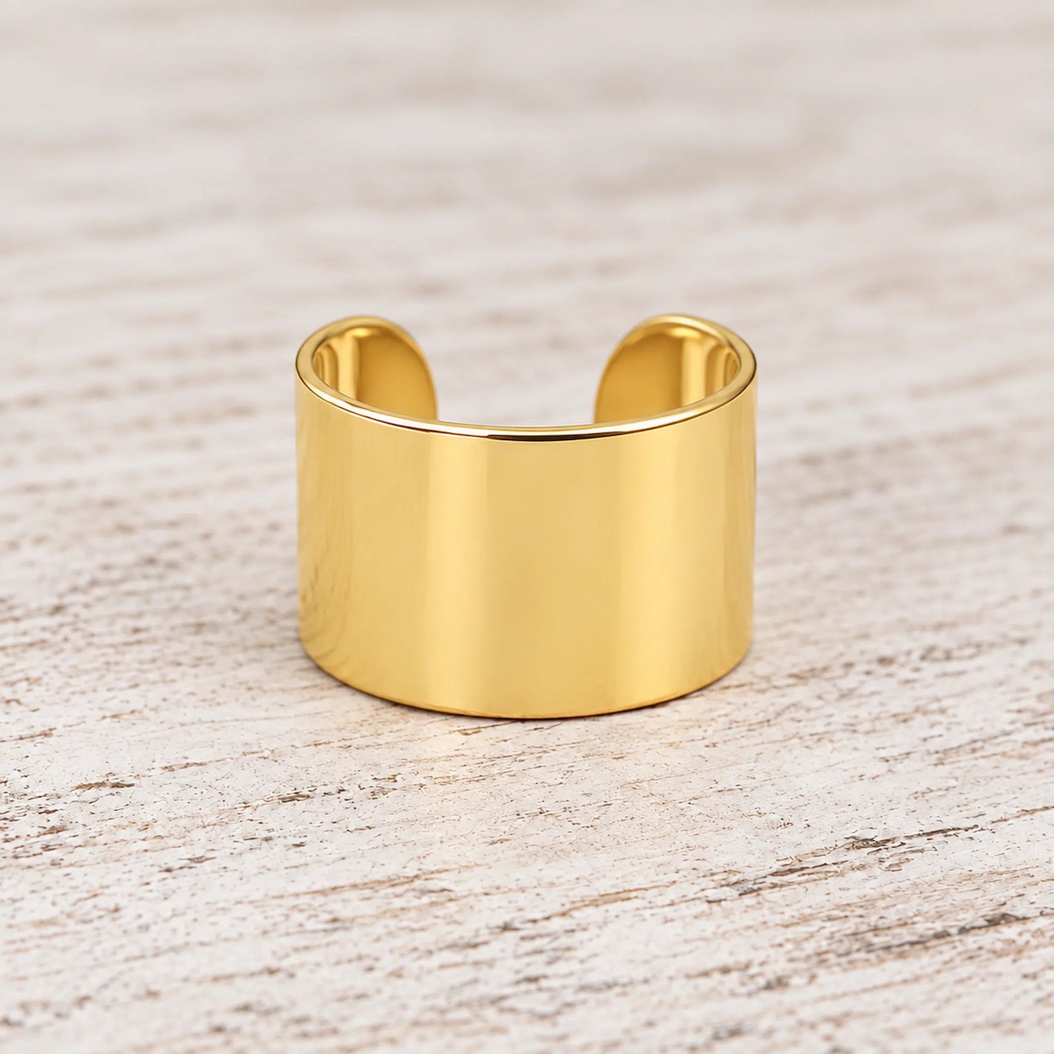 Gold ear cuff on a white background with blurred flowers in the background - gold waterproof jewellery by indie and harper