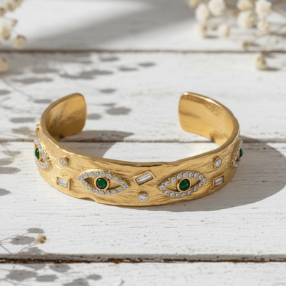 Gold bracelet with green gemstones and diamond accents on a light wooden surface.