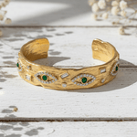 Gold bracelet with green gemstones and diamond accents on a wooden surface
