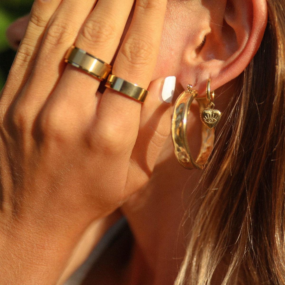 close up of woman wearing gold waterproof jewellery including gold evil eye heart charm huggie earrings in stainless steel