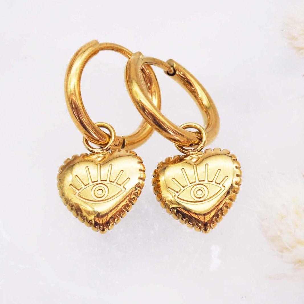 Waterproof Stainless Steel Gold Evil Eye Heart Charm Huggie Earrings on a white surface