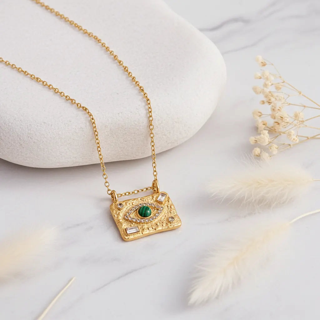 Gold Evil Eye necklace with a malachite centre eye displayed on a smooth white stone with soft florals.