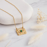 Gold Evil Eye necklace with a malachite centre eye displayed on a smooth white stone with soft florals.
