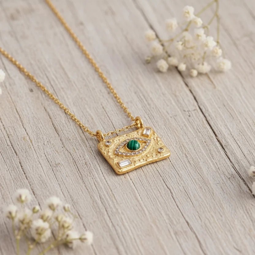 Gold Evil Eye necklace with a malachite centre eye displayed on a smooth white stone with soft florals.