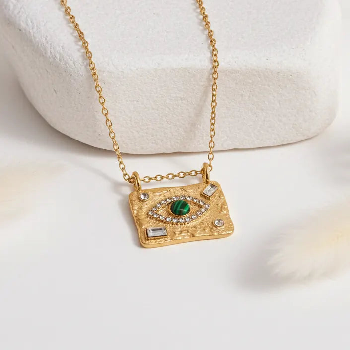 Close-up of gold Evil Eye necklace featuring a round malachite stone and sparkling cubic zirconia details on a textured pendant.