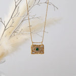 Gold Evil Eye pendant necklace with malachite centre stone hanging against soft cream feathers.