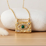 Textured gold Evil Eye necklace with cubic zirconia and malachite stone displayed on a warm wooden surface.