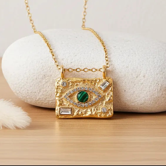 Textured gold Evil Eye necklace with cubic zirconia and malachite stone displayed on a warm wooden surface.