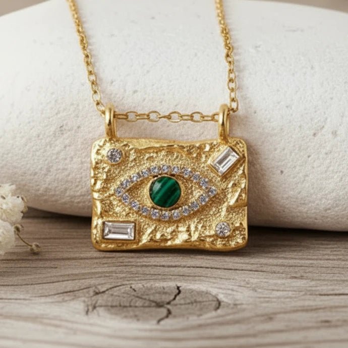 Textured gold Evil Eye necklace with cubic zirconia and malachite stone displayed on a warm wooden surface.