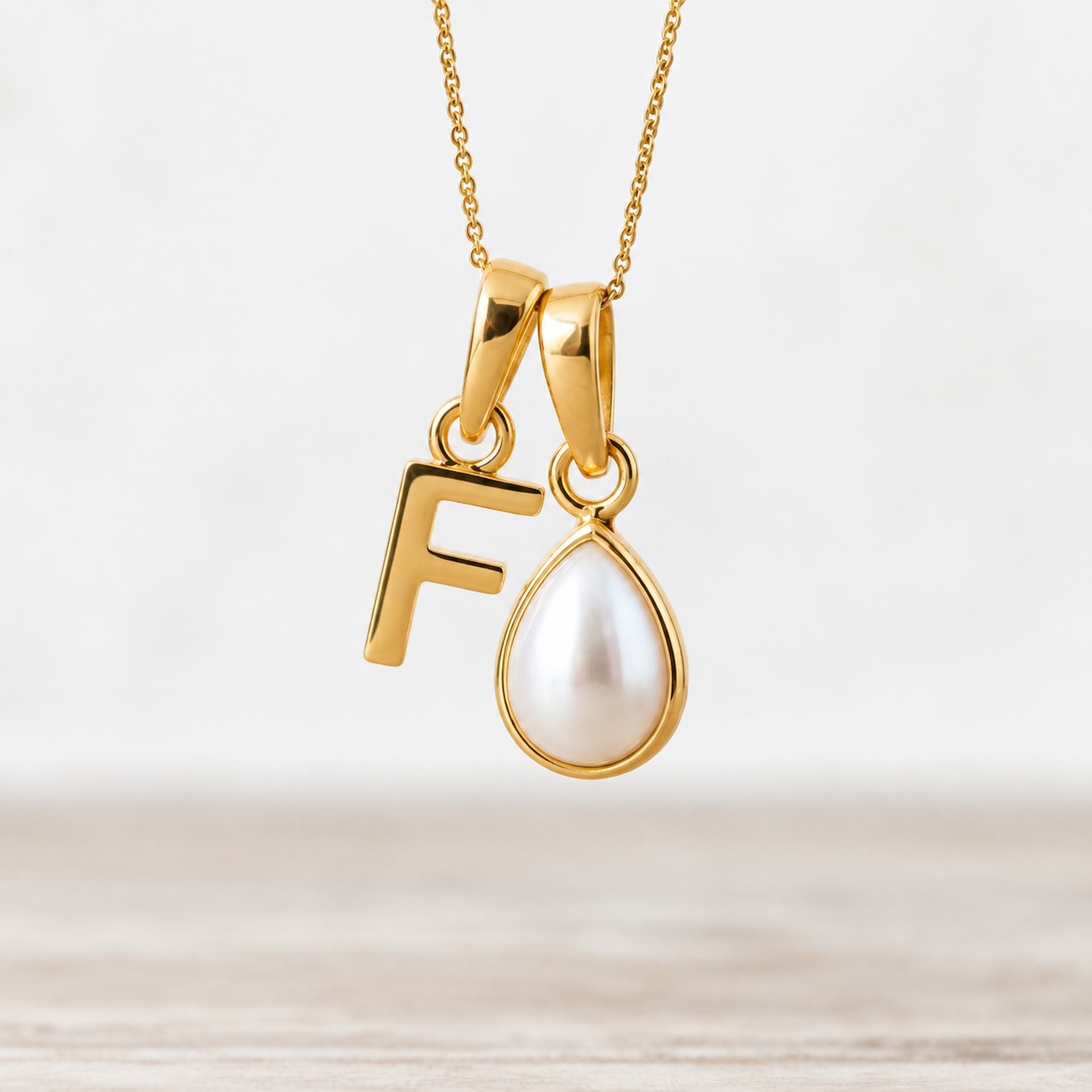 Gold June birthstone necklace with a pear-shaped natural mother of pearl pendant and letter 'F' charm.