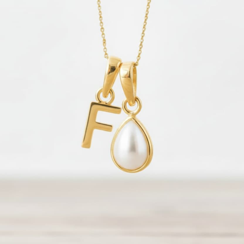 Gold necklace with 'F' pendant and pearl pendant on a light background