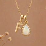 Gold Initial F Pendant and October birthstone Natural Opal Necklace against a warm background
