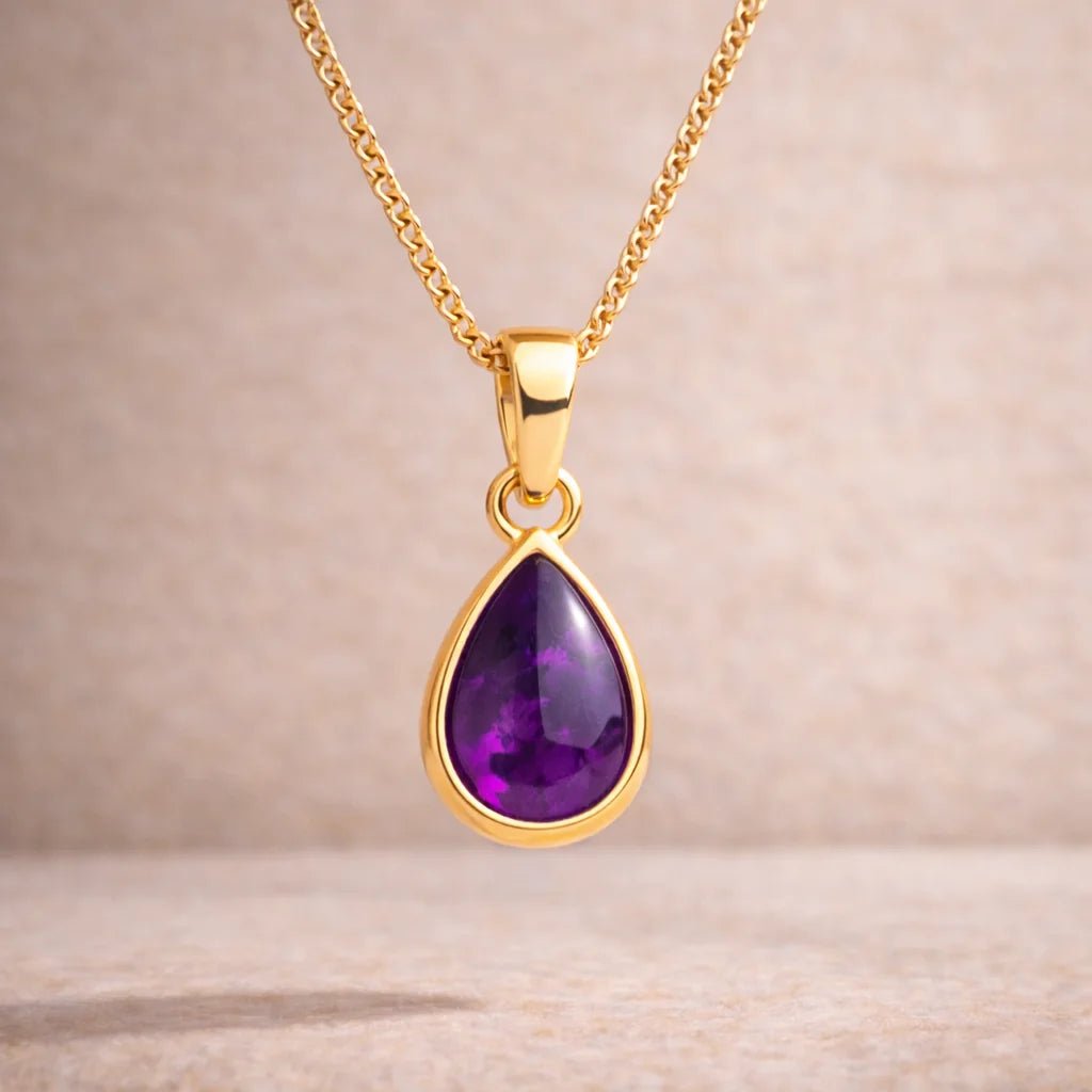 Gold necklace with a purple teardrop natural amethyst pendant on a beige background