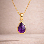 Gold necklace with a purple teardrop natural amethyst pendant on a beige background