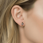 Close-up of a person wearing a teardrop-shaped earring with a purple gemstone.