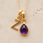 Gold double pendant necklace with a february birthstone purple teardrop amethyst gemstone pendant and letter 'Z' charm on a beige background